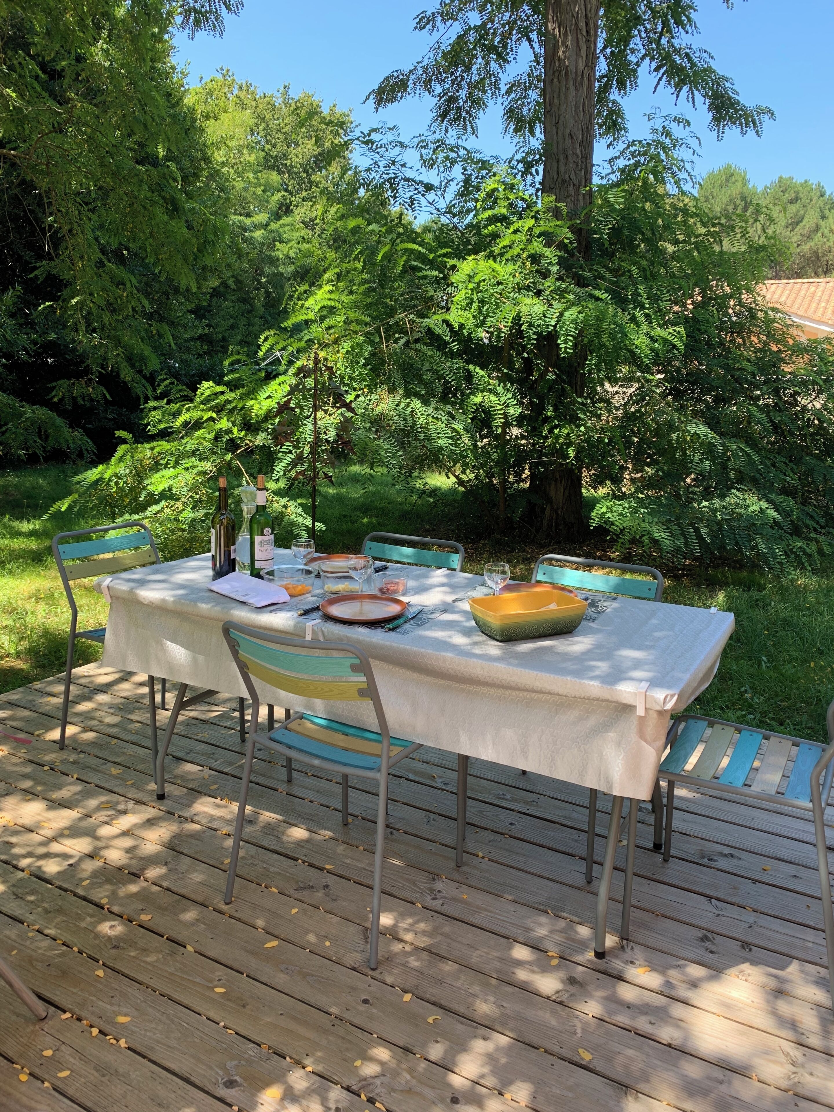 Un ensemble de table et de chaises pour prendre les repas en plein air, installé sur une terrasse en bois, le tout entouré d’une végétation luxuriante.