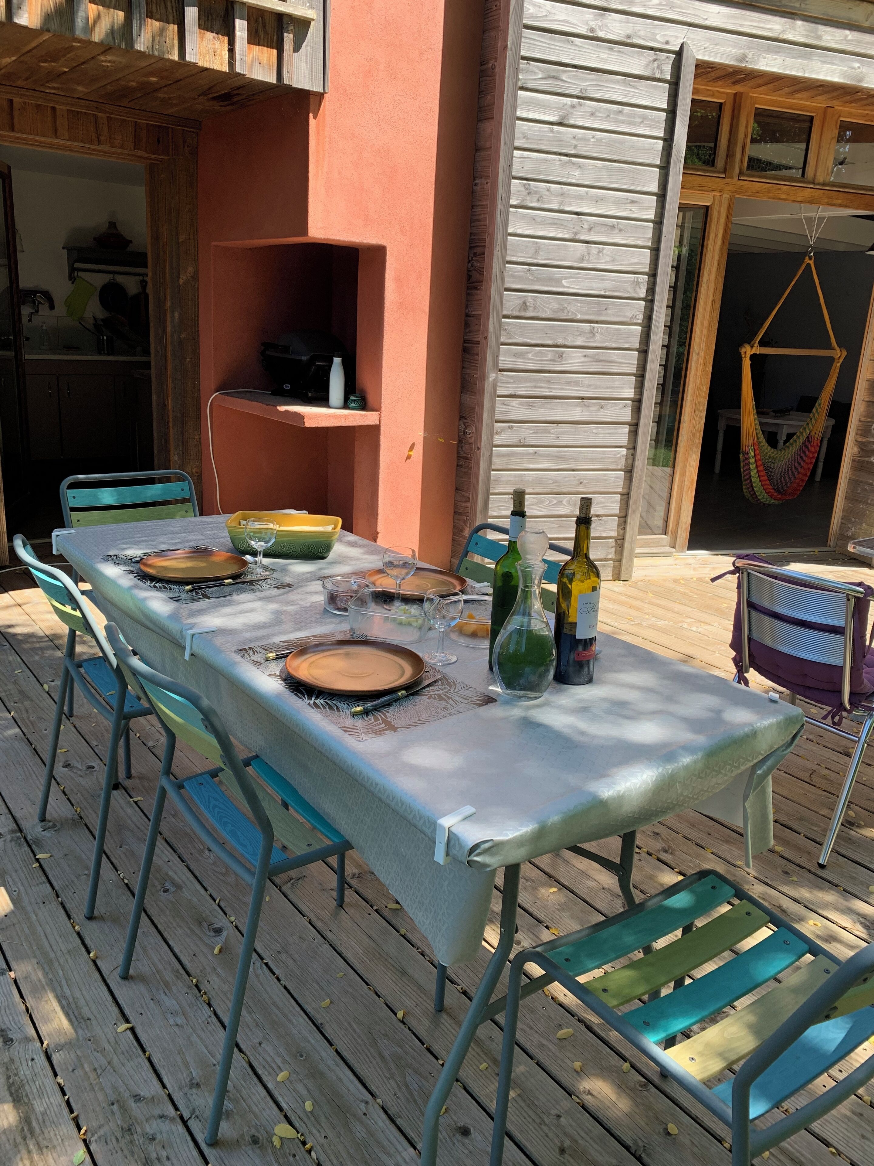 Eine Holzterrasse mit Esstisch, Gartenstühlen und einer Hängematte.