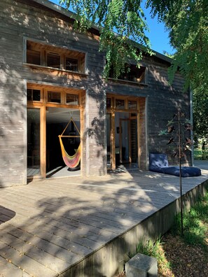 A modern wooden house with large windows, a hammock, and a deck. - Maison Bioclimatique (Vendays-Montalivet)