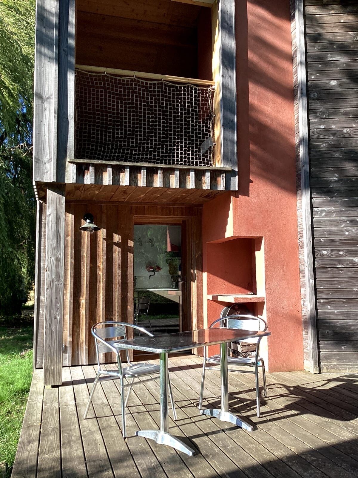 Une terrasse en bois avec deux chaises en métal et une petite table, une clôture en bois et un mur rouge.