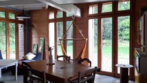 Een eetruimte met een houten tafel en stoelen, grote ramen en een hanglamp.