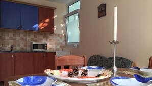 Une cuisine avec une table à manger dressée pour le repas, agrémentée d’un centre de table décoratif composé de pommes de pin et d’une bougie.