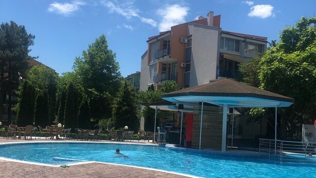 Une piscine dotée d’une zone abritée, entourée d’arbres et bordée d’un immeuble à plusieurs étages.