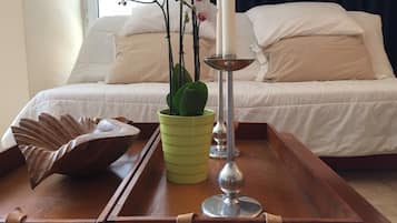 A neatly arranged bedroom with a bed, a bedside table with a green vase, a decorative bowl, and a tall candle holder.