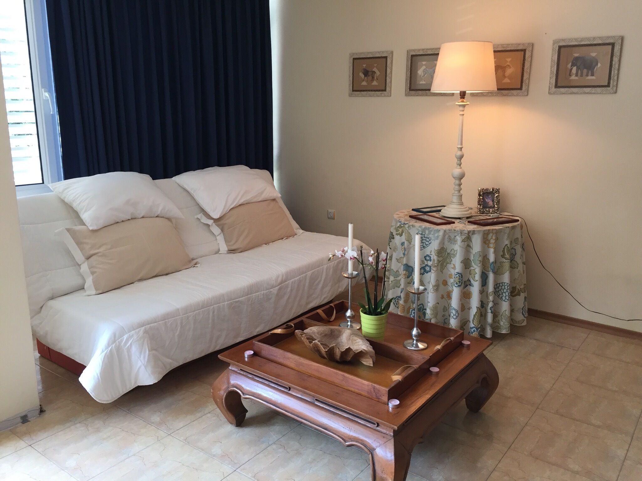 A cozy room with a bed, a wooden coffee table with a tray, a lamp, and framed pictures on the wall.