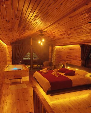 A wooden cabin interior with a bed, a bench, a small table, and a bathtub.