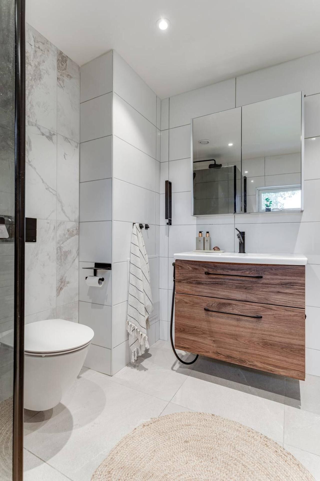 Ein modernes Badezimmer mit Toilette, Holzwaschtisch und Spiegel sowie Marmorrückwand.