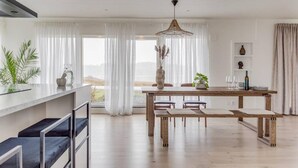 Une cuisine moderne dotée d’un grand îlot central, d’une table à manger en bois et de chaises. Les fenêtres offrent une vue sur une étendue d’eau.