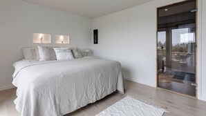Une chambre avec un grand lit, deux lampes fixées au mur, une fenêtre avec vue et une porte-fenêtre coulissante.