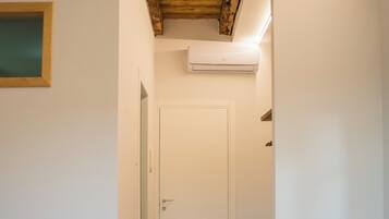 A bedroom with a bed, a wooden bench, an air conditioning unit, and a door leading to another room.