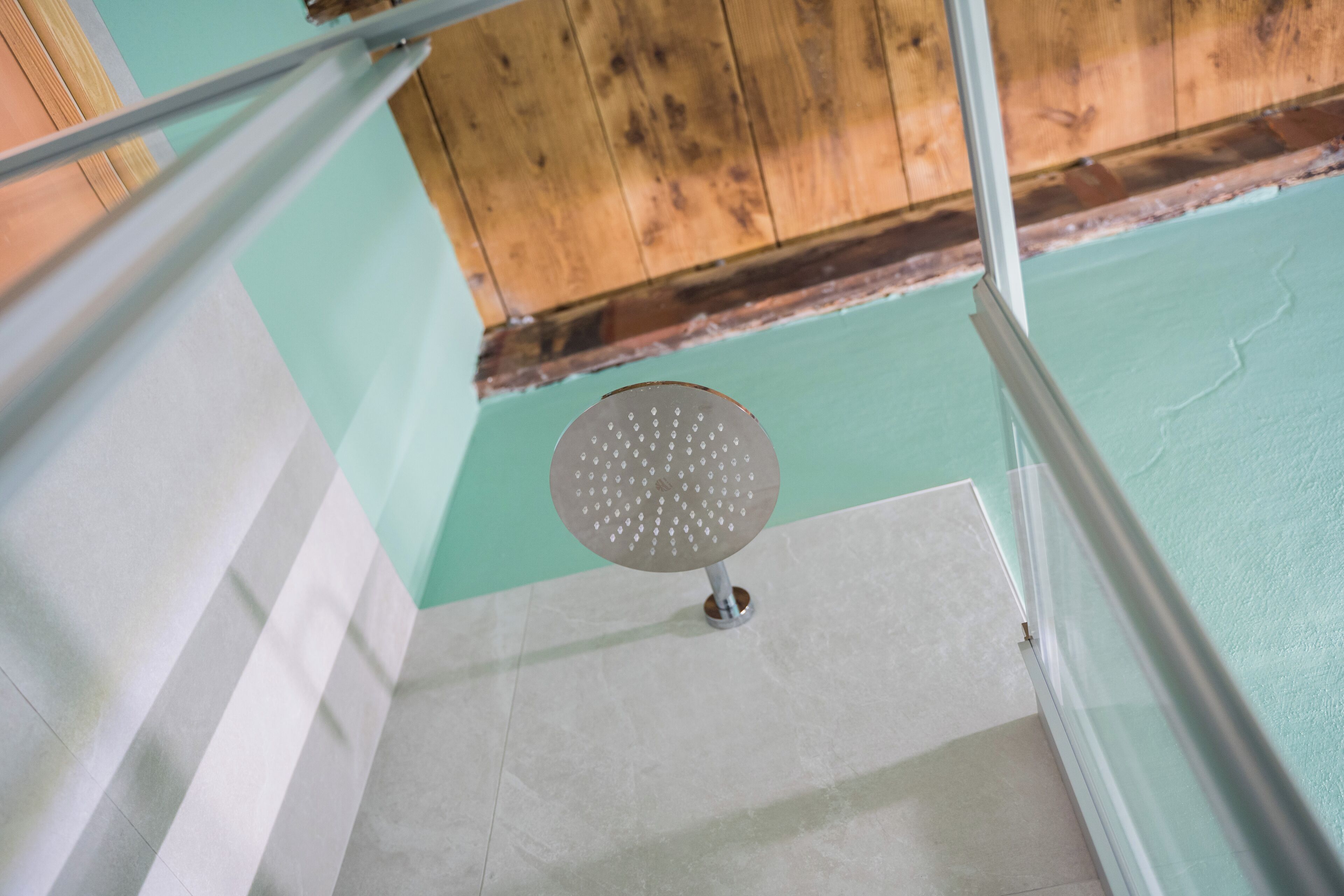 A showerhead in a bathroom with a wooden ceiling and a teal wall.
