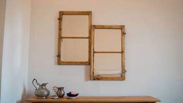 Two wooden-framed mirrors on a wall, a wooden table with a metal pitcher, a small vase, and a decorative item.