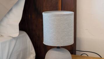 Uma mesa de cabeceira de madeira com uma luminária, uma cama com roupa de cama branca e uma cabeceira de madeira.