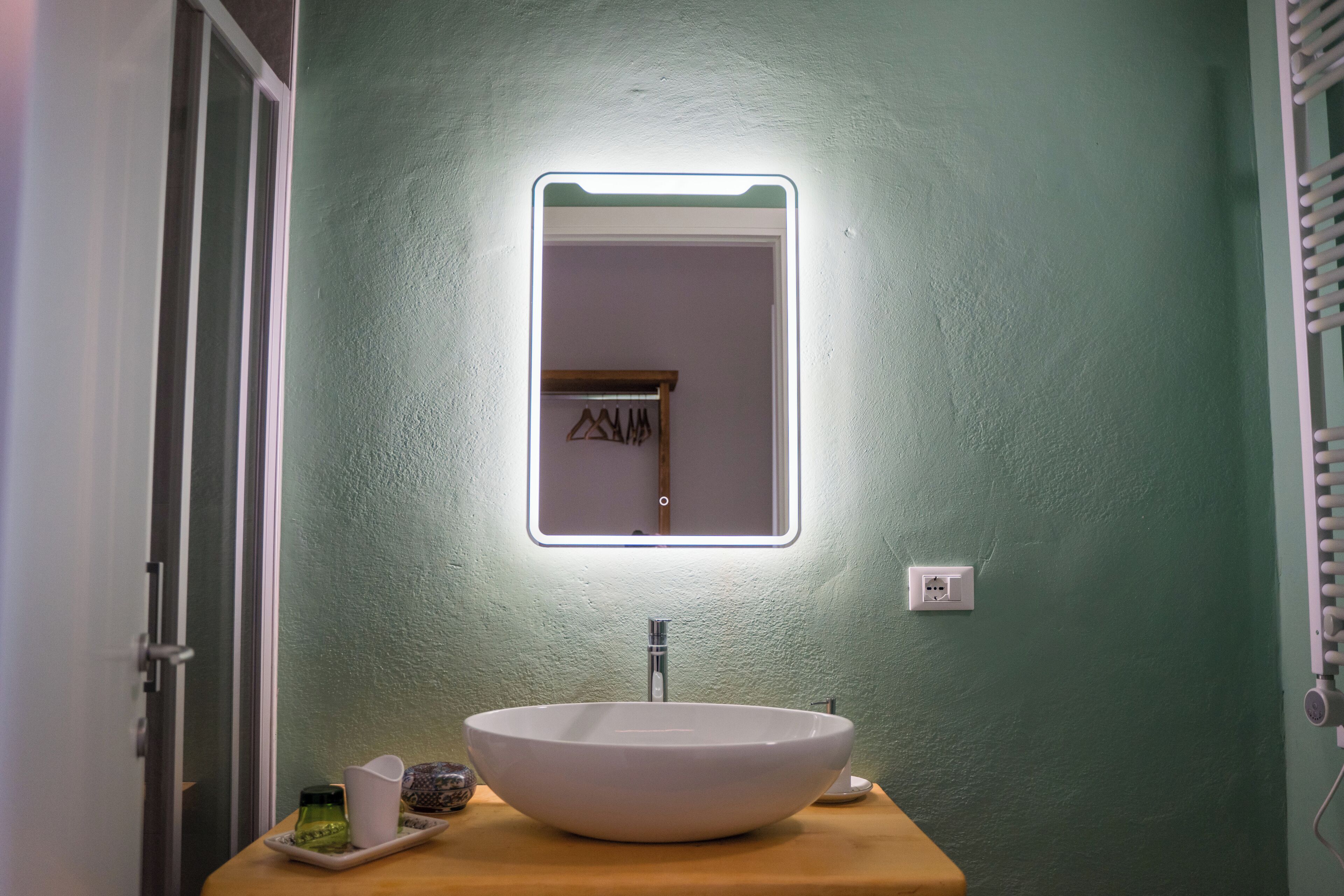 Un baño con un lavabo blanco tipo pedestal, un espejo con luz y una encimera de madera.