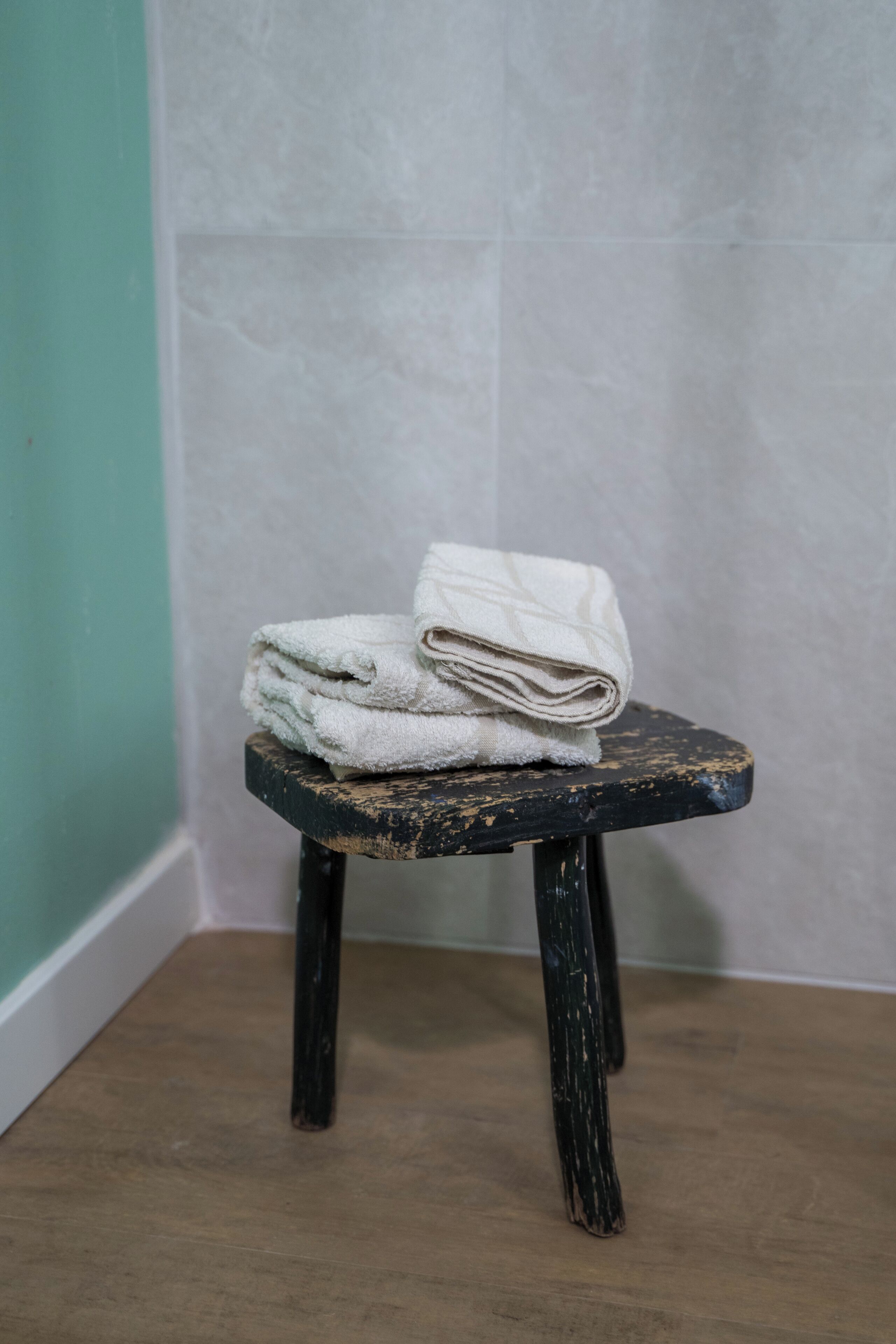 A small wooden stool with a stack of white towels placed on top.