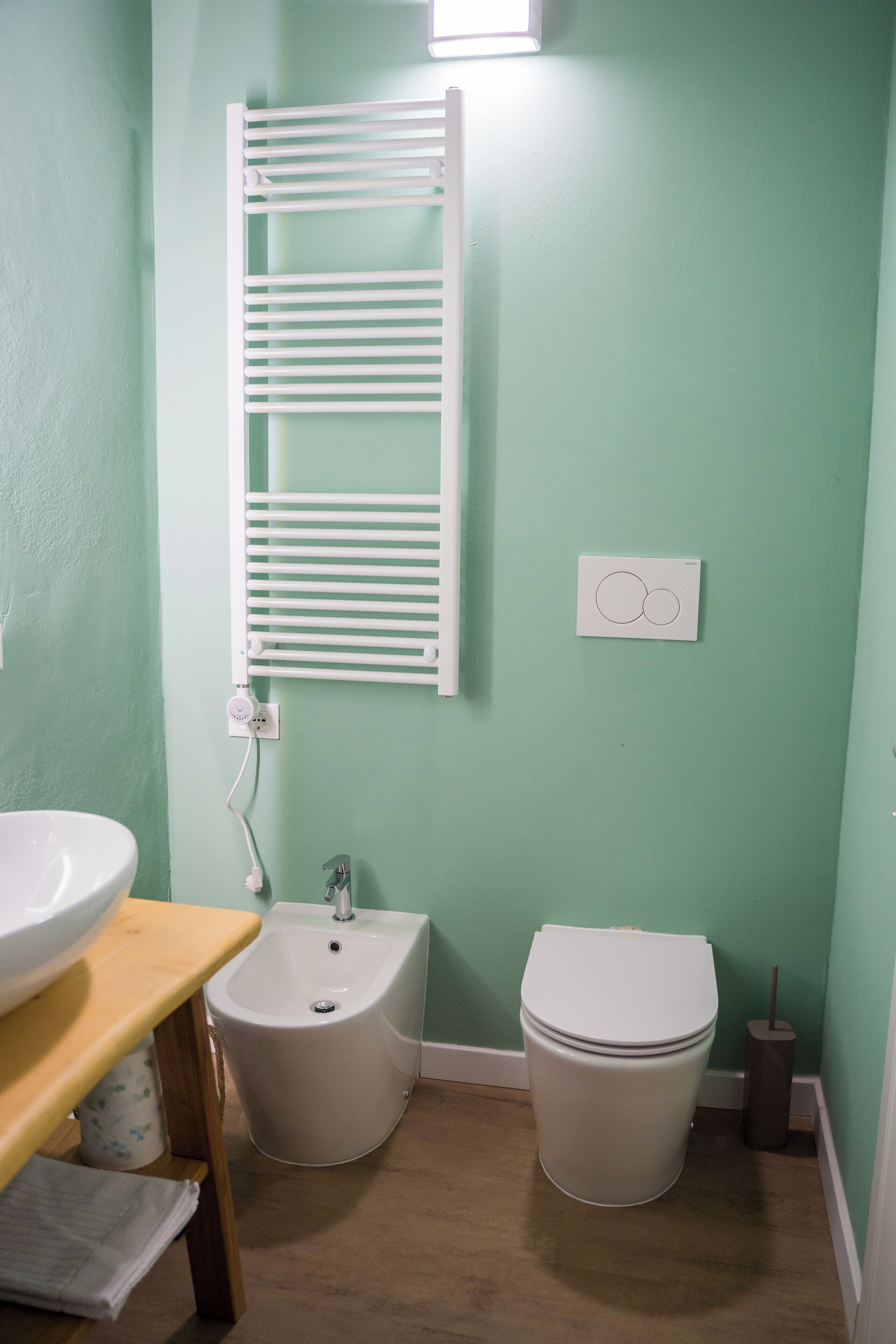 Ein Badezimmer mit grüner Wand, einem weißen Handtuchhalter, einem Bidet, einer Toilette und einem Waschbecken mit Holzausleger.