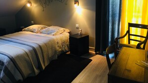 Ein Schlafzimmer mit Bett, Nachttisch, Sessel, Schreibtisch und Wand mit Herz-Dekoration.