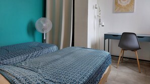 A bedroom with a bed, a desk, a chair, a fan, and a curtain. - Agréable T2 Avec vue sur la mer (Leucate)