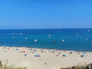 Une plage où il y a beaucoup de monde, des parasols colorés et des bateaux sur l’eau.