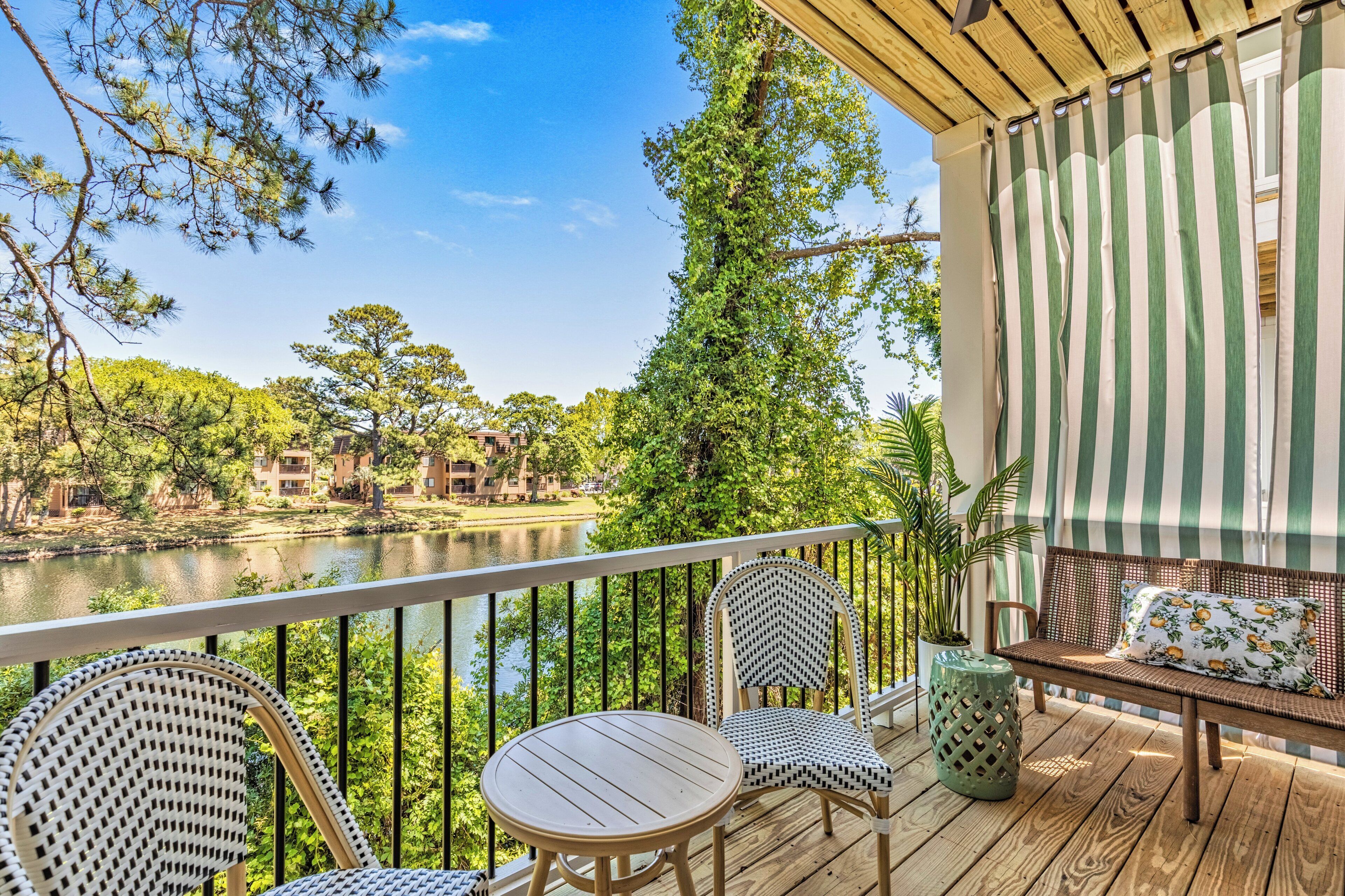 A wooden deck with a view of a river and trees, a striped awning, and outdoor furniture.