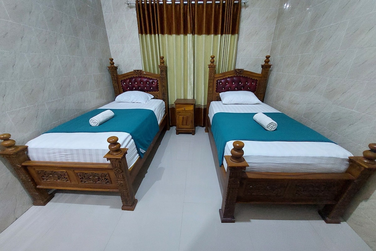 A room with two wooden beds, each with a headboard and footboard, and a small wooden nightstand between them.