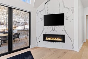 Un salon moderne avec une cheminée, une grande fenêtre et une vue sur un espace extérieur enneigé.