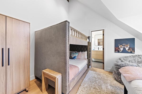 Une chambre avec un lit superposé, une armoire en bois, un petit tabouret en bois, un tapis moelleux et un tableau accroché au mur.