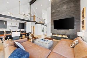 Een moderne zithoek met een ruime leren bank, een flatscreen televisie aan een stenen muur en een open haard.