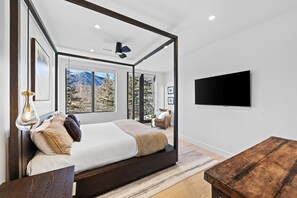 A modern bedroom with a four-poster bed, large windows, a flat-screen TV, and a wooden coffee table.
