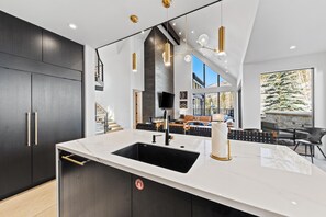 Een moderne keuken met een groot eiland, donkere kasten en uitzicht op de woonkamer.
