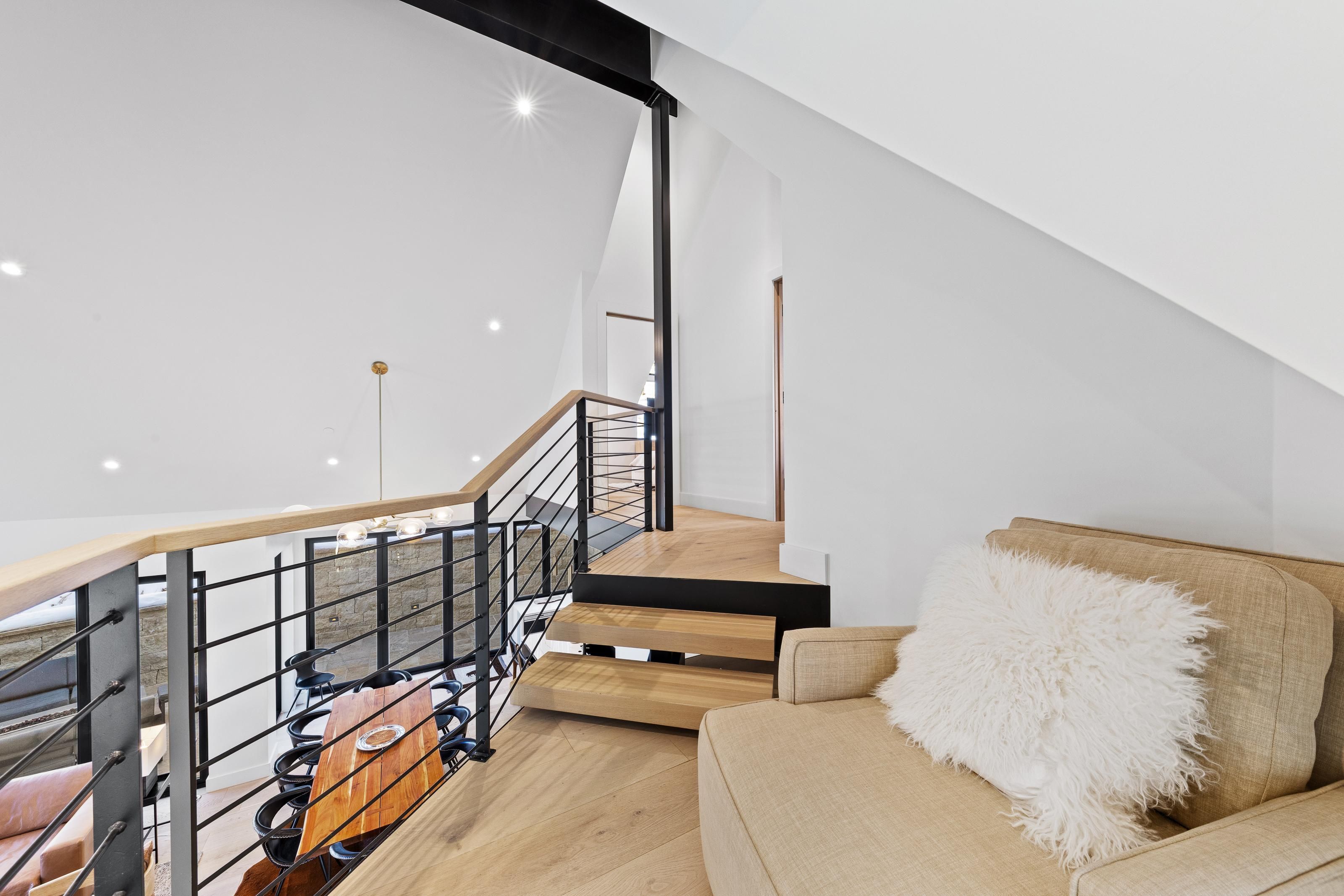 A modern interior with a staircase, wooden flooring, a sofa with a fluffy pillow, and a dining area with a wooden table and chairs.