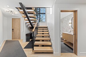 Un intérieur moderne avec un escalier en bois, une salle de bain ouverte dotée d’un comptoir en marbre et une porte donnant sur une autre pièce.