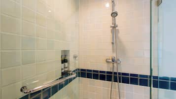 Une salle de bain avec des carreaux blancs et bleus, une cabine de douche en verre et une barre d’appui.