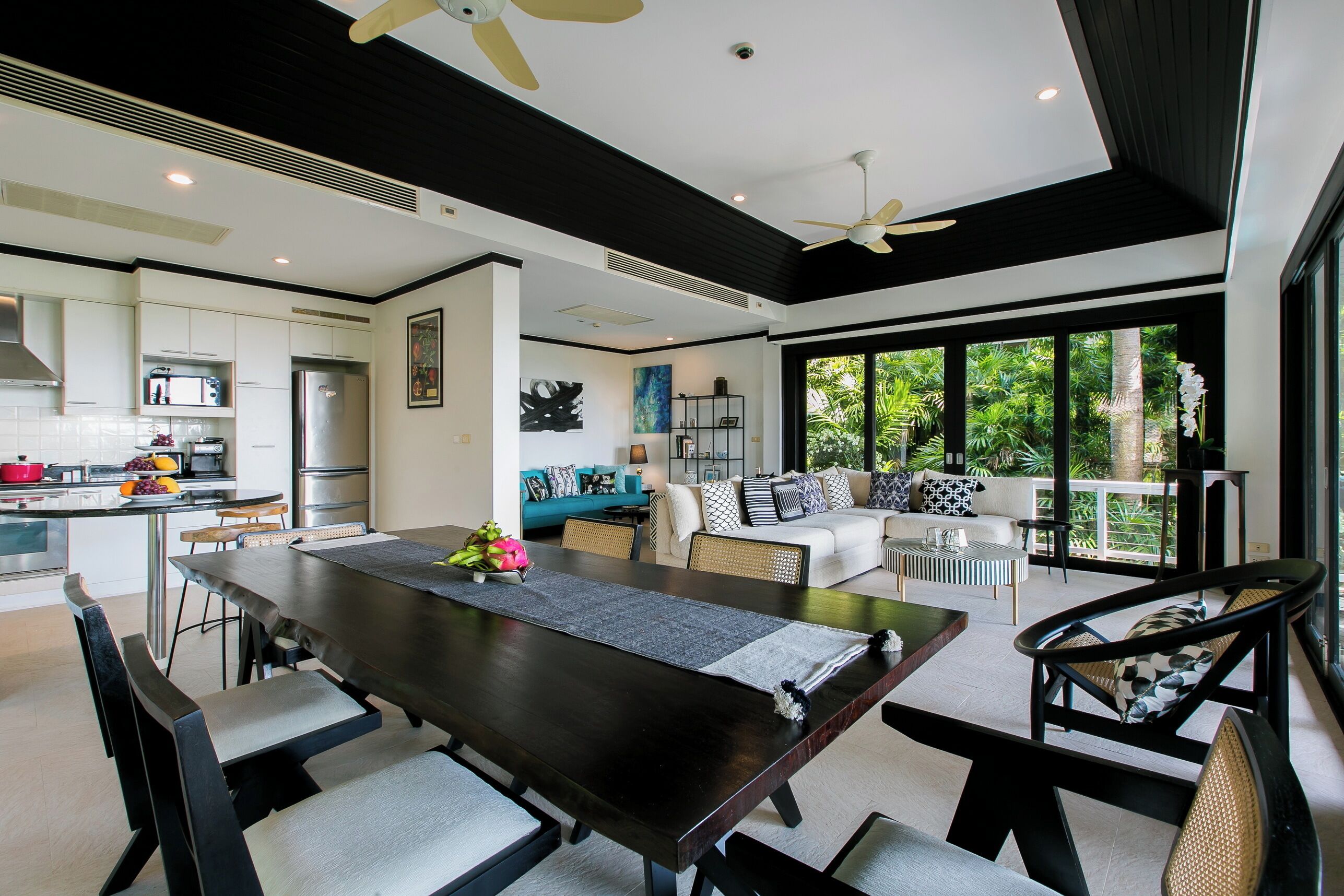 A modern kitchen with a dining area, large windows, and a ceiling fan.