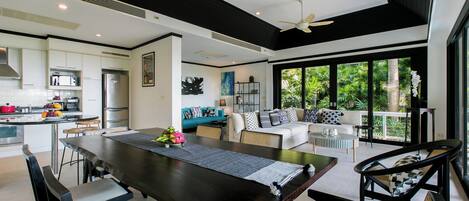 A modern kitchen with a dining area, large windows, and a ceiling fan.