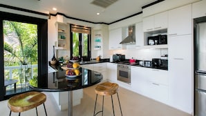 A modern kitchen with white cabinetry, a black countertop, and a central island with stools. - Katamanda Villa Jade A6 Seaview Kata Beach (Muang Phuket)