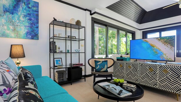 A modern living room with a teal sofa, a black coffee table with magazines and apples, a black bookshelf, and a large TV on a black cabinet. - Katamanda Villa Jade A6 Seaview Kata Beach (Muang Phuket)