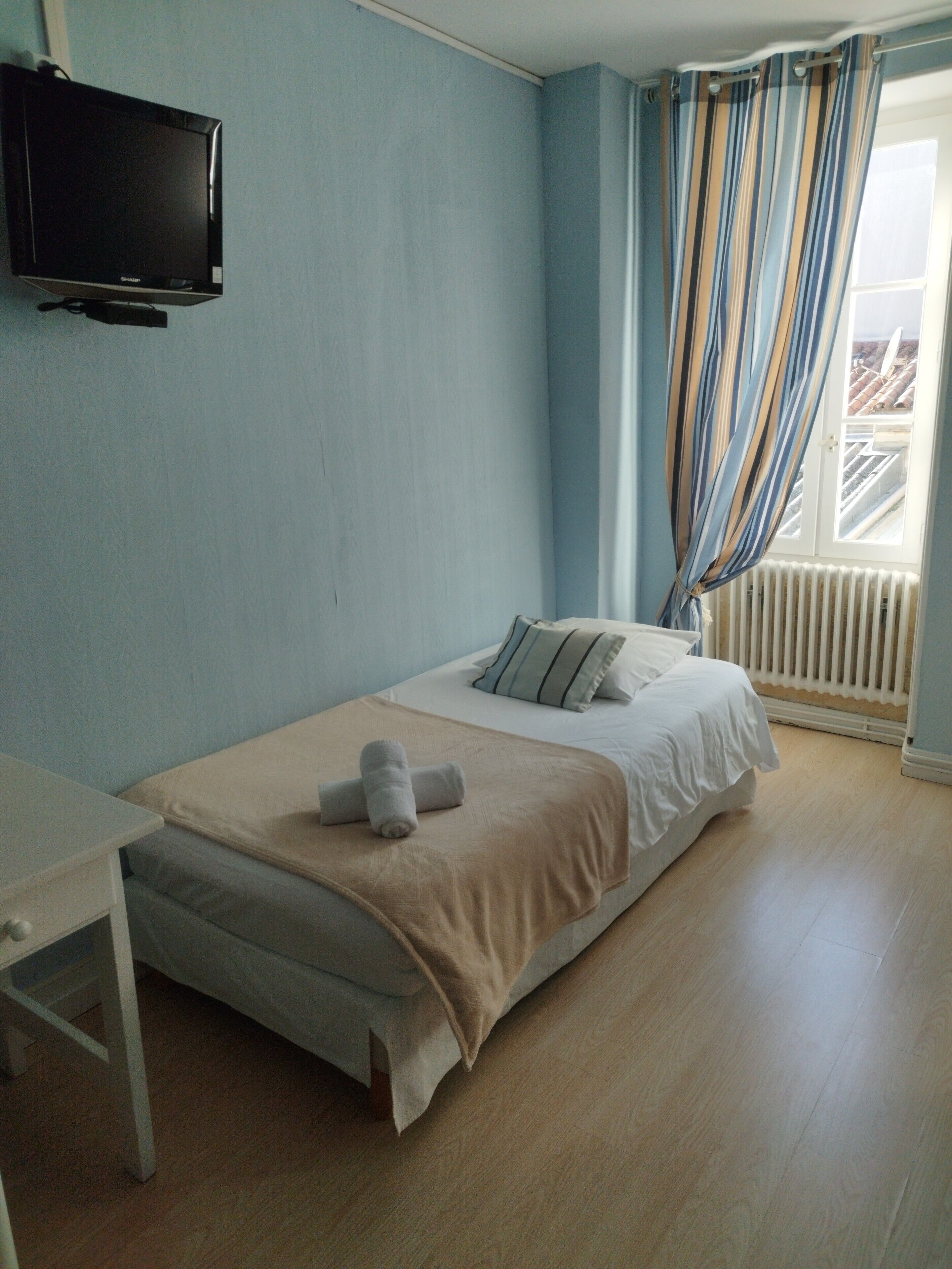 A bedroom with a bed, a TV mounted on the wall, a window with curtains, and a radiator.