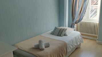 A bedroom with a bed, a TV mounted on the wall, a window with curtains, and a radiator.