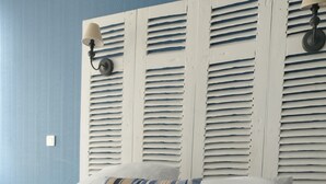 A neatly made bed with rolled white towels, a striped pillow, and white bedding against a blue wall with a wooden headboard. - Hôtel les Thermes (Jonzac)