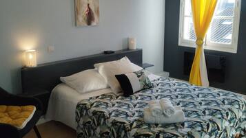 Un dormitorio con cama, una mesita de noche, una silla, un cuadro en la pared y una ventana con cortinas.