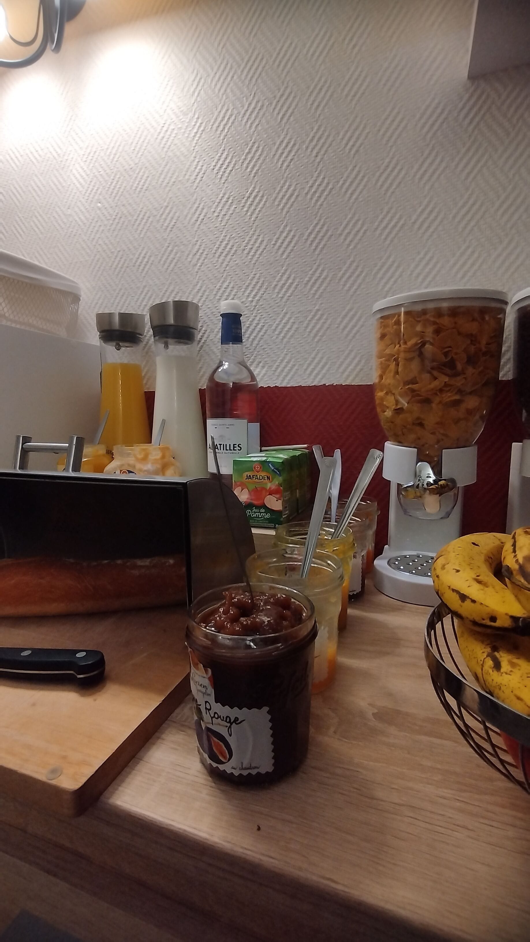 Una encimera de cocina con diversos alimentos y condimentos, incluyendo frascos de mermelada, una licuadora y una cesta de plátanos.
