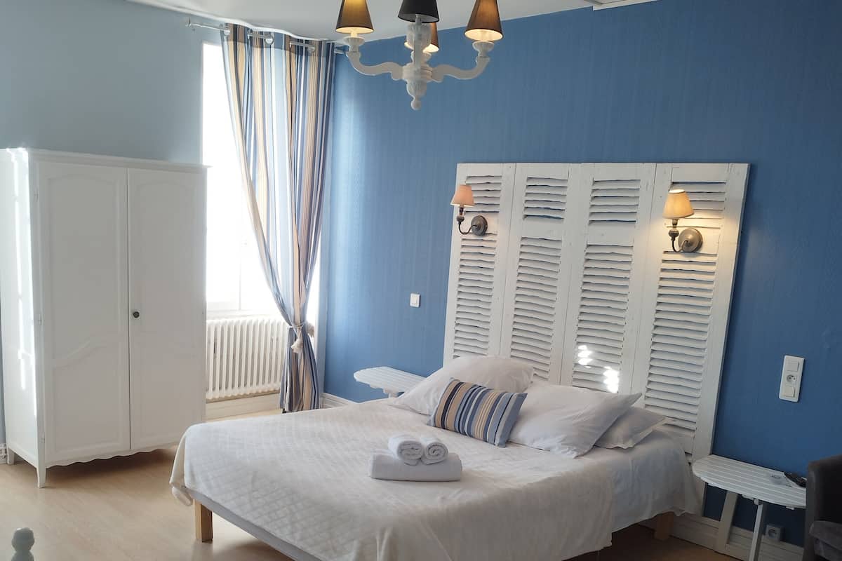 Um quarto com uma cama, um guarda-roupa branco, uma mesinha e uma cadeira.