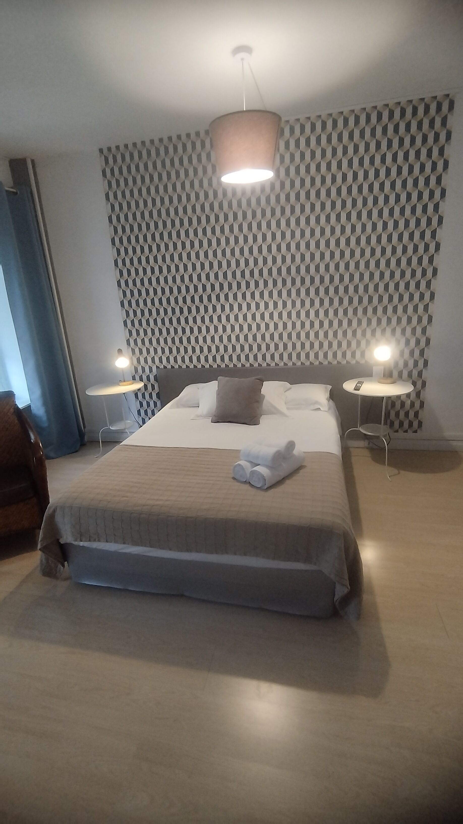 A modern hotel room with a large bed, two bedside tables with lamps, a patterned wall, and a ceiling light.