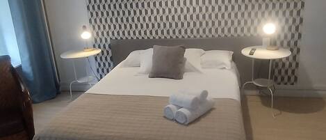 A modern hotel room with a large bed, two bedside tables with lamps, a patterned wall, and a ceiling light.