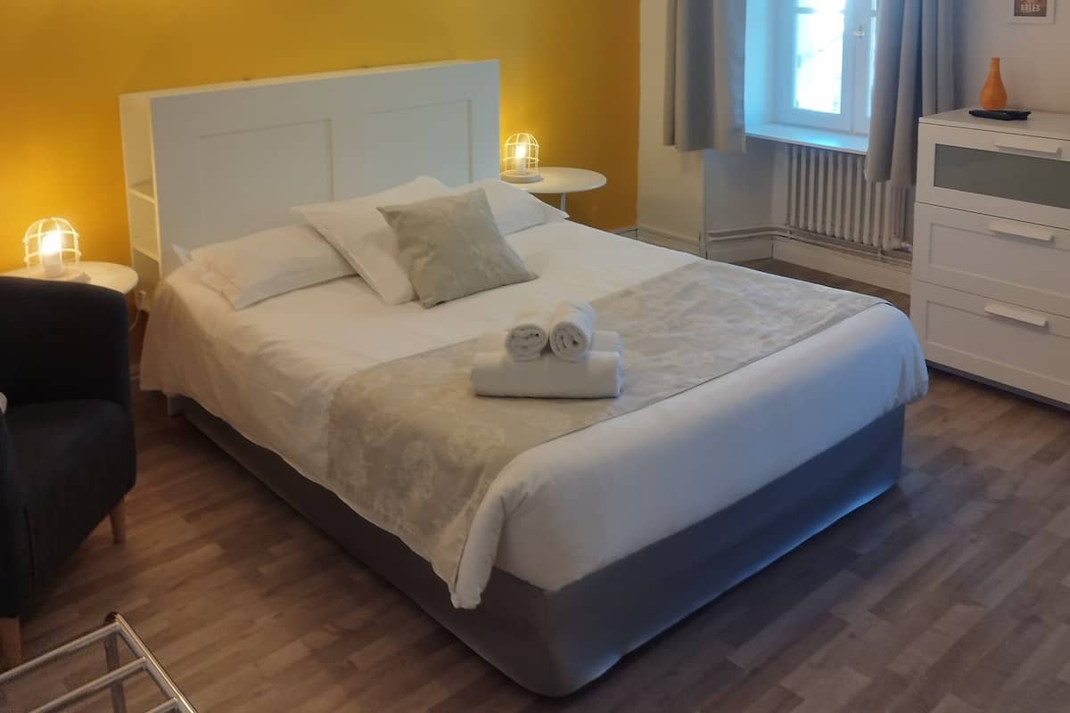 Quarto bem arrumado com uma cama grande, luminárias de cabeceira, mesa de cabeceira, uma cadeira, cômoda e uma janela com cortinas.