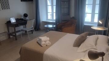 Habitación de hotel con cama, escritorio, silla, televisor y ventana con cortinas.
