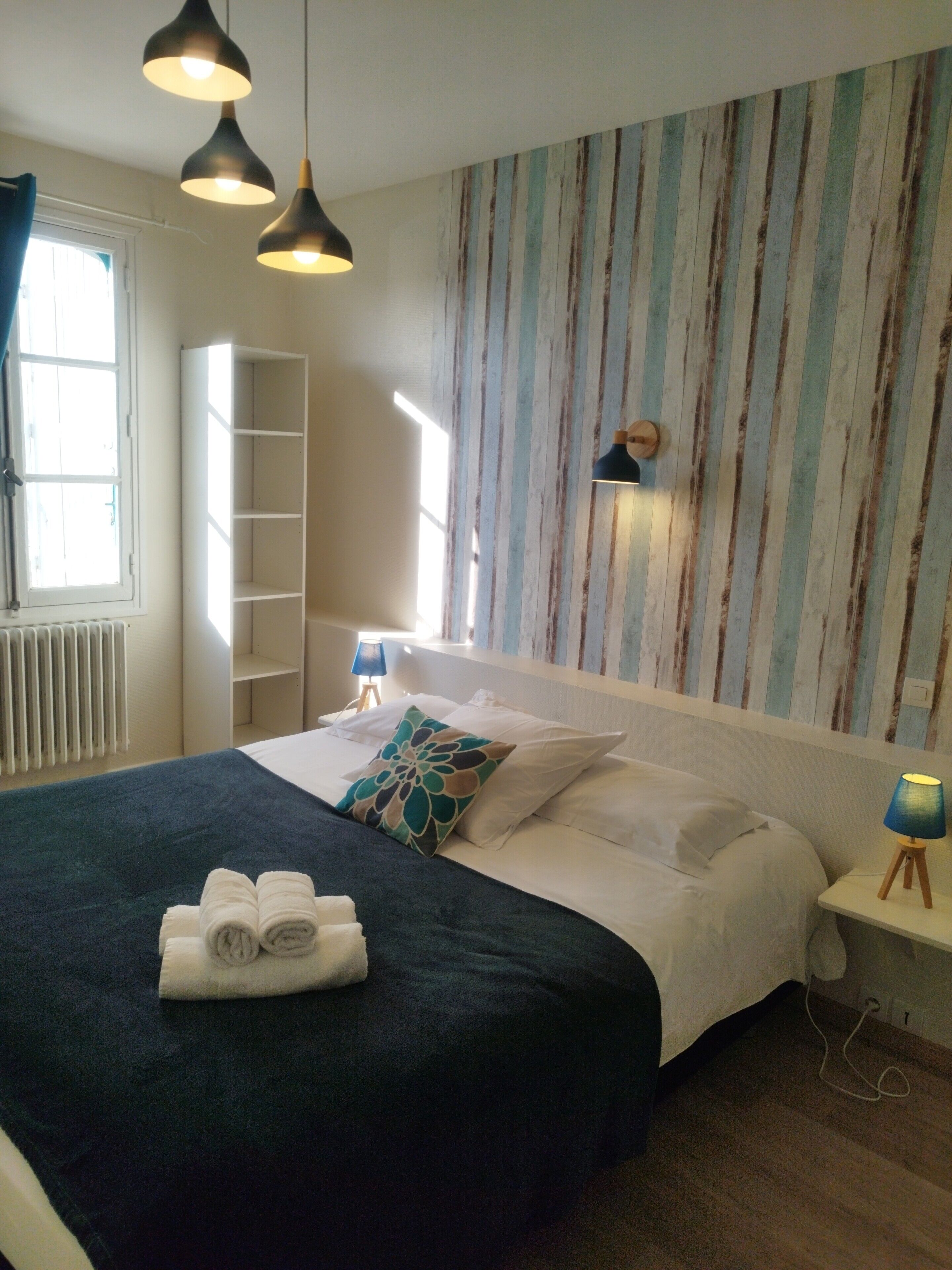 A neatly made bed with a dark blue bedspread and white pillows, a bedside lamp, and a striped wall behind the bed.