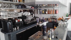 Una zona de bar con una máquina de café, una grifo de cerveza y estantes llenos de botellas de licores y vasos.