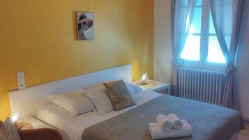 A hotel room with a large bed, a nightstand, a chair, a wall-mounted picture, and a window with curtains.